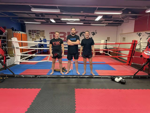 Tre tränare poserar framför ringen. Herman, Henrik och Tony poserar framför thaiboxningsringen.