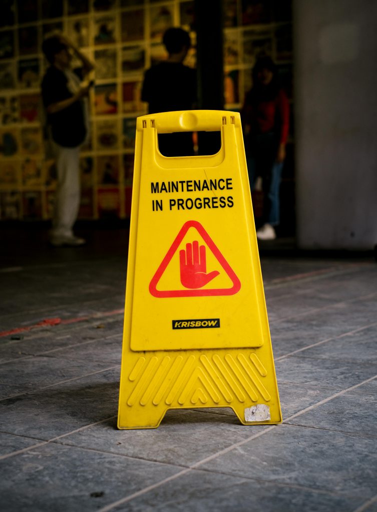 Bright yellow 'Maintenance in Progress' sign on tiled pavement in Jakarta, Indonesia.